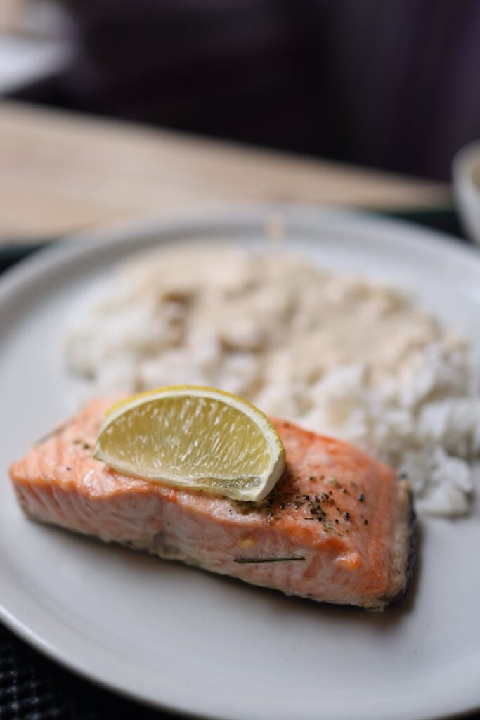 Tasty salmon fillet topped with lime slice, served with creamy rice on a white plate.